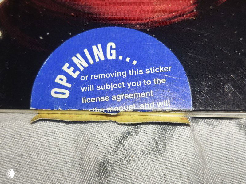 Крупный план круглой запечатанной наклейки с английской надписью о том, что вскрытие или снятие означает принятие лицензионного соглашения.