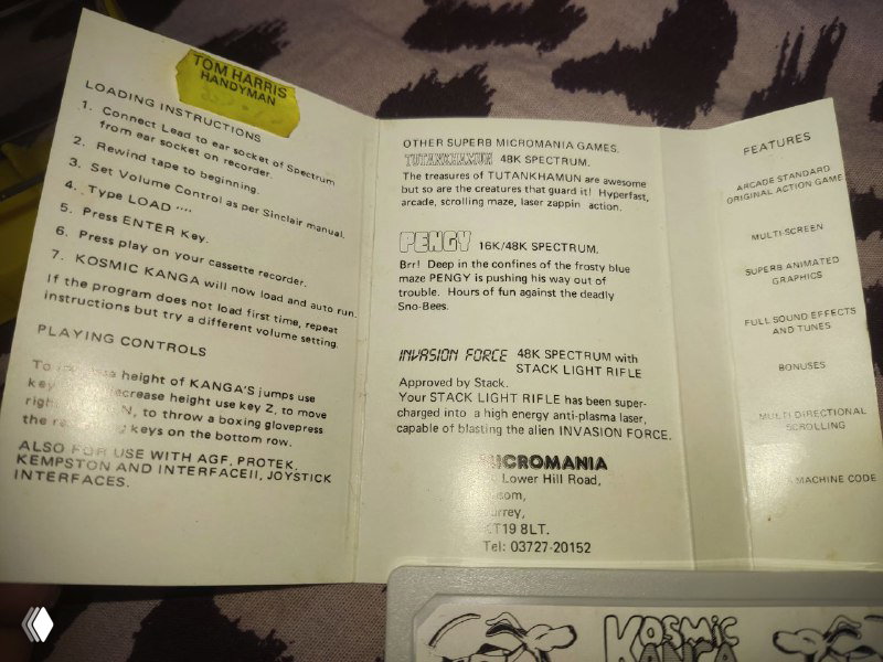Развёрнутый буклет/инструкция от игры Kosmic Kanga, бумажные страницы с текстом и списком управления; кассета видна внизу кадра.