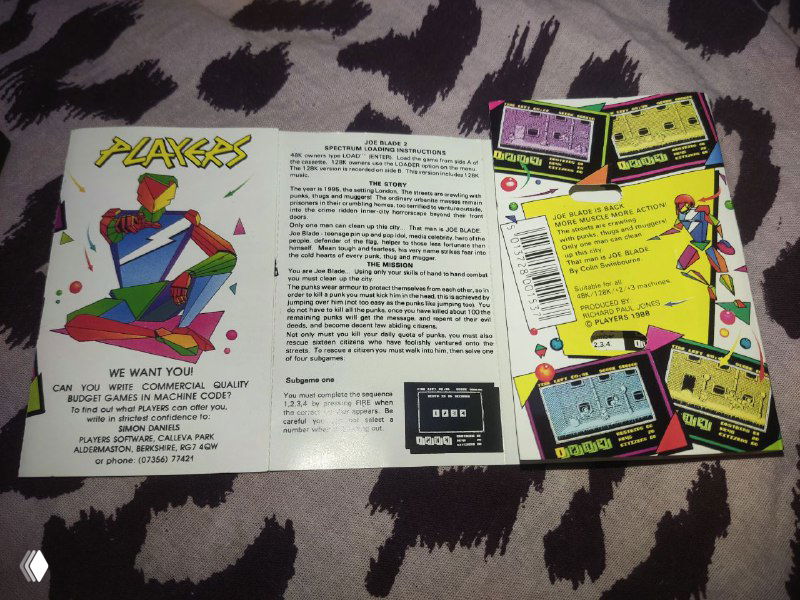 Буклет и обложка издания Joe Blade II в раскрытом виде; цветные иллюстрации, рекламные вставки и логотип Players на бумажном вкладыше, виден дизайн упаковки.