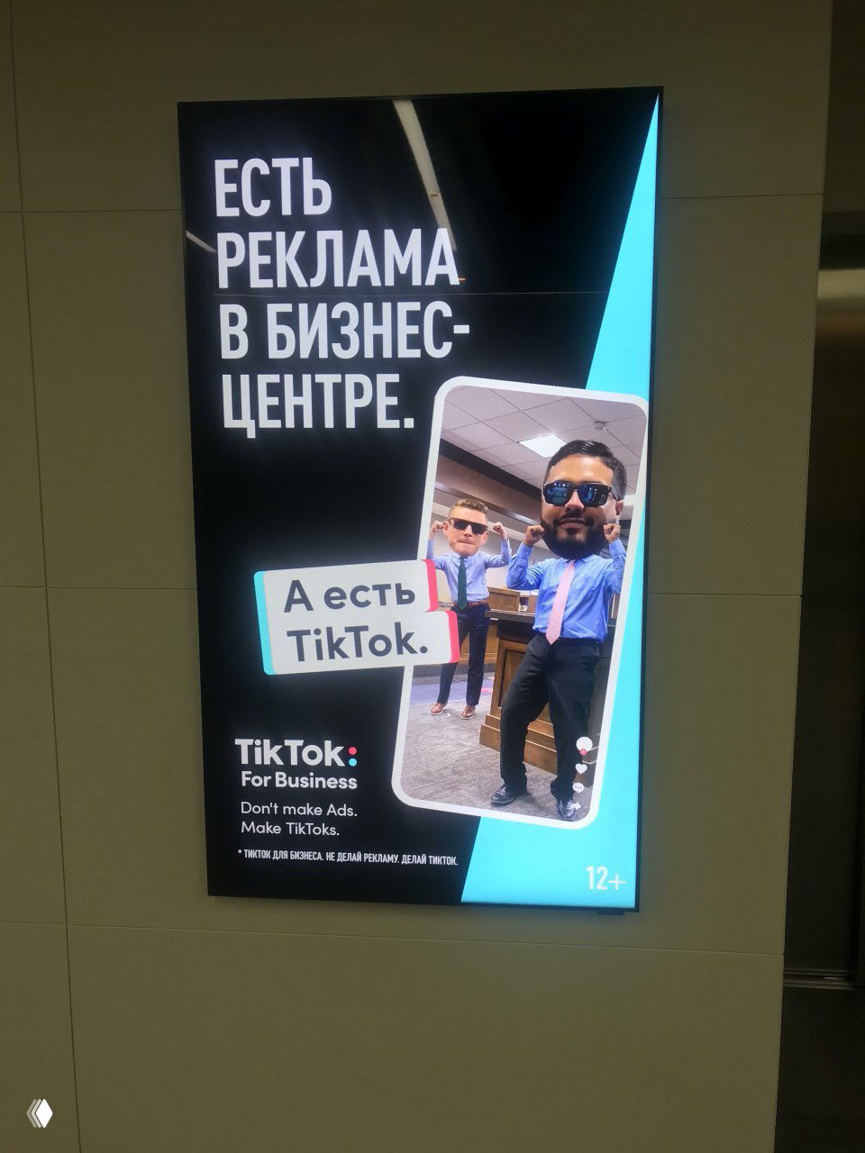 Световой рекламный экран в бизнес-центре с текстом «Есть реклама в бизнес-центре. А есть TikTok» и кадром из инфид-ролика с двумя мужчинами.
