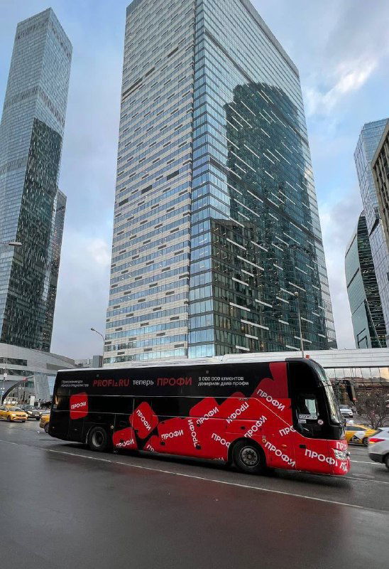 Красный брендированный автобус с повторяющимся логотипом «Профи» на фоне стеклянных высоток Москва-Сити, демонстрирующий уличную кампанию бренда.