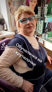 Портрет парикмахера Елены в салоне: кадр из Reels, она в ярких очках на фоне полок с товарами и профессиональной рабочей обстановкой.