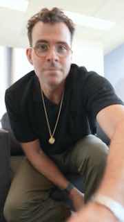 Человек в очках делает вертикальное селфи в интерьере офиса; кадр показывает торс и лицо в полуразвороте, иллюстрация темы Reels и репостов