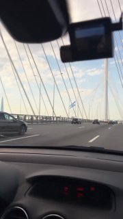 Вид из салона автомобиля на дорожное полотно и кабельный мост; приборная панель внизу кадра и трафик на дороге, контекст съёмки ролика для Буше