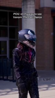 Кадр из ролика: человек на улице в шлеме Венома, поверх кадра белый текст POV и подпись про поход смотреть Venom; скриншот TikTok с уличным фоном.