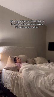 Кадр вертикального видео: человек лежит в кровати и вспоминает внезапную доставку Poppi вендинговой машины в середине ночи, интерьер спальни виден.