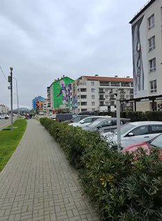 Городская улица с многоэтажками и раскрашенным фасадом; кадр снят глазами при прогулке по тротуару и показывает урбанистический фон.