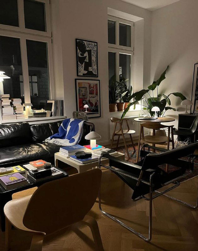 Ночной интерьер с диваном, журнальным столом и несколькими плакатами на стене; тёплое освещение подчёркивает атмосферу помещения.