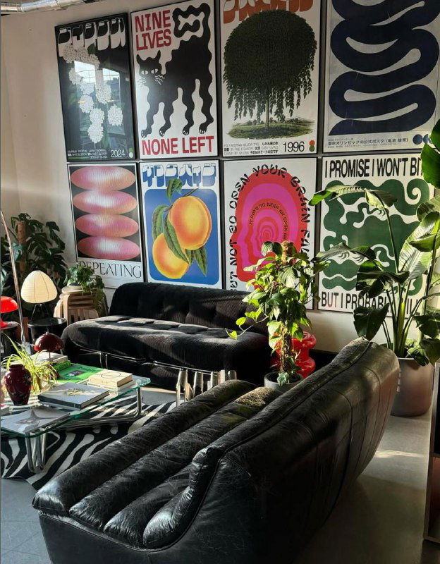 Комната с чёрным диваном и стеной, полностью покрытой разноформатными постерами — наглядный пример стен-галерей в домашних интерьерах.