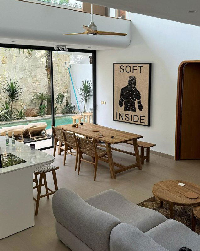 Светлая столовая зона с постером «SOFT INSIDE» и видом во двор; сочетание плаката и мебели показывает коммерческий потенциал простых афиш.