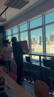 Кадр из рилса в офисном пространстве: люди переносят коробки у панорамных окон, визуал о совместных активностях и коллабах между брендами.