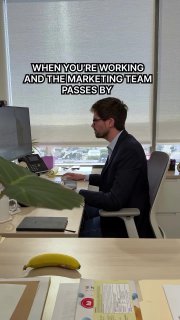 Офисный сотрудник в очках сидит за столом, окно за спиной; на кадре текст про «когда команда маркетинга проходит мимо» — мем о восприятии маркетинга внутри компании.