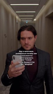 Вертикальный видеокадр: мужчина в коридоре держит телефон и делает селфи-видео, на экране виден наложенный юмористический текст.