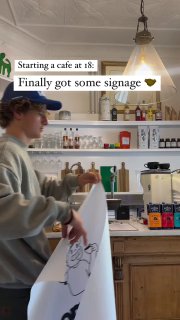 Интерьер кафе: барная стойка, полки с бутылками и напитками, молодой человек за прилавком — кадр процесса и повседневной работы заведения.