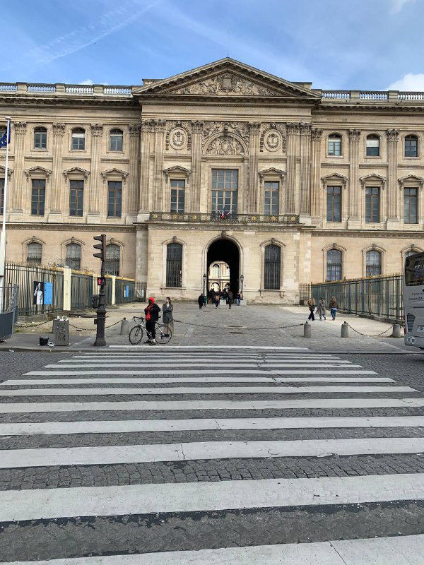 Входный фасад исторического здания в Париже со ступенями и пешеходным переходом на переднем плане в ясный весенний день.