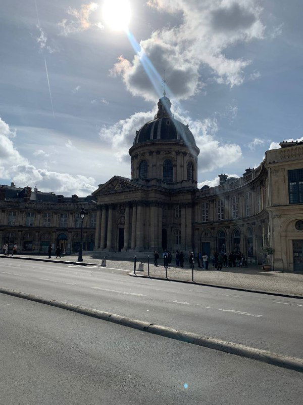 Монументальное купольное здание под солнечным светом; на переднем плане пустая улица и мягкие тени от городских объектов.