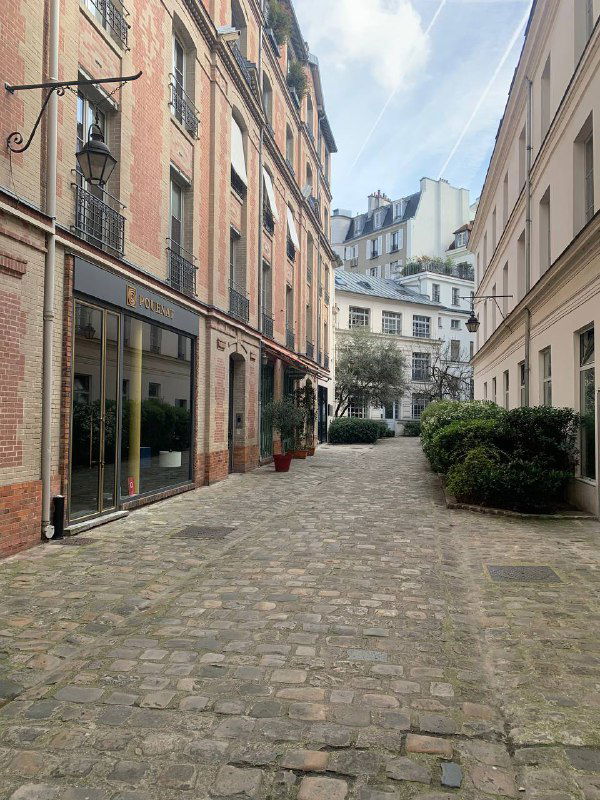Уютный парижский дворик с брусчаткой, узкими домами и зелёными насаждениями — типичная тихая улочка центра города для прогулок.