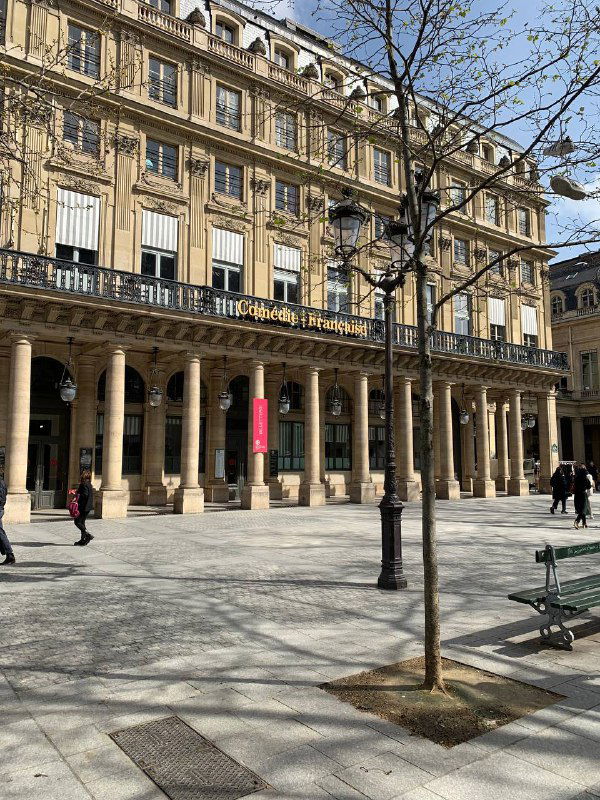 Площадь с колоннадами и фасадами, небольшие деревья на тротуаре и мягкие тени — пример классической городской архитектуры Парижа.