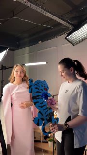 Студийный кадр: автор поста и ещё одна женщина держат синий арт-объект «Большая киса» на фоне светового оборудования и белой съемочной сцены.