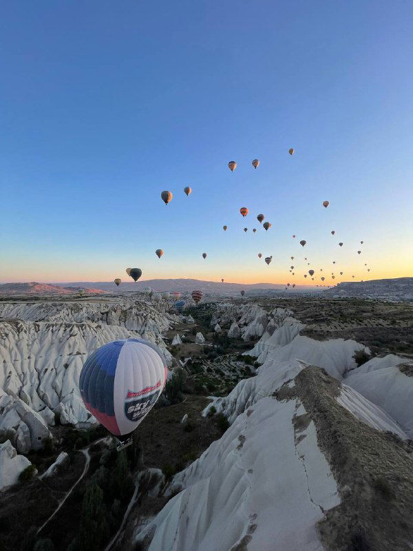 Утреннее небо с множеством воздушных шаров над уникальным каменным ландшафтом Каппадокии; вид на полёт шаров и долины при рассвете.