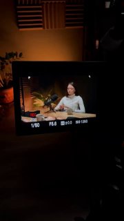 Съёмка через экран камеры: женщина-эксперт сидит в студии во время записи, видны свет, микрофон и часть декорации