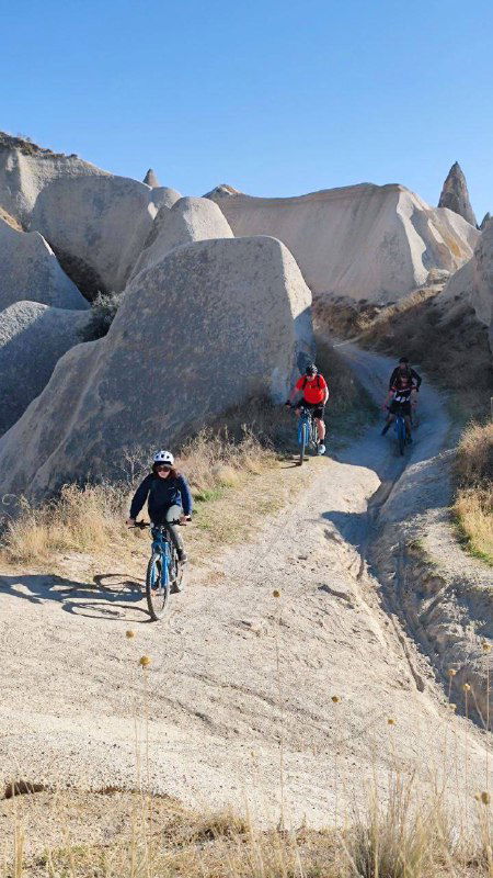 Группа велосипедистов спускается по узкой тропе между мягкими вулканическими скалами и ущельями в яркий солнечный день.