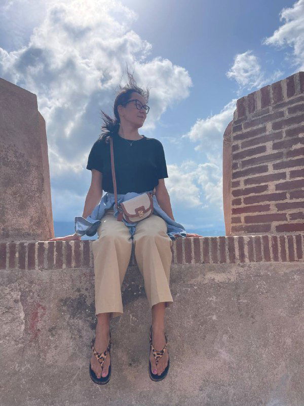 Автор или туристка сидит на каменной стене укрепления с видом на небо и море, расслабленная поза на фоне летнего пейзажа Эльбы.