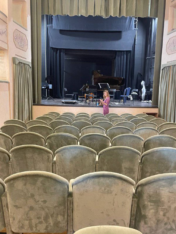 Интерьер маленького провинциального театра: пустые бархатные кресла, сцена и рояль — камерная сцена с историческим занавесом.