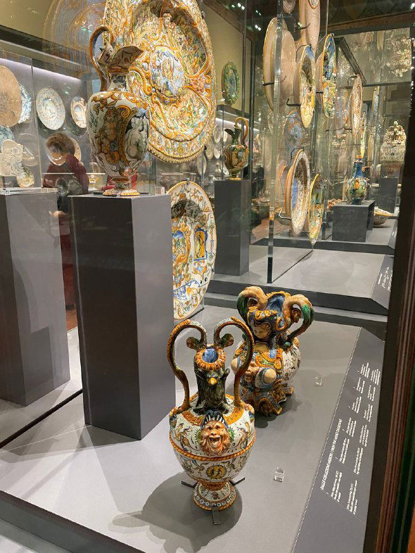 Ещё одна витрина с расписной керамикой и формами посуды в музее Барджелло, отражение других экспонатов на стекле и интерьер зала.