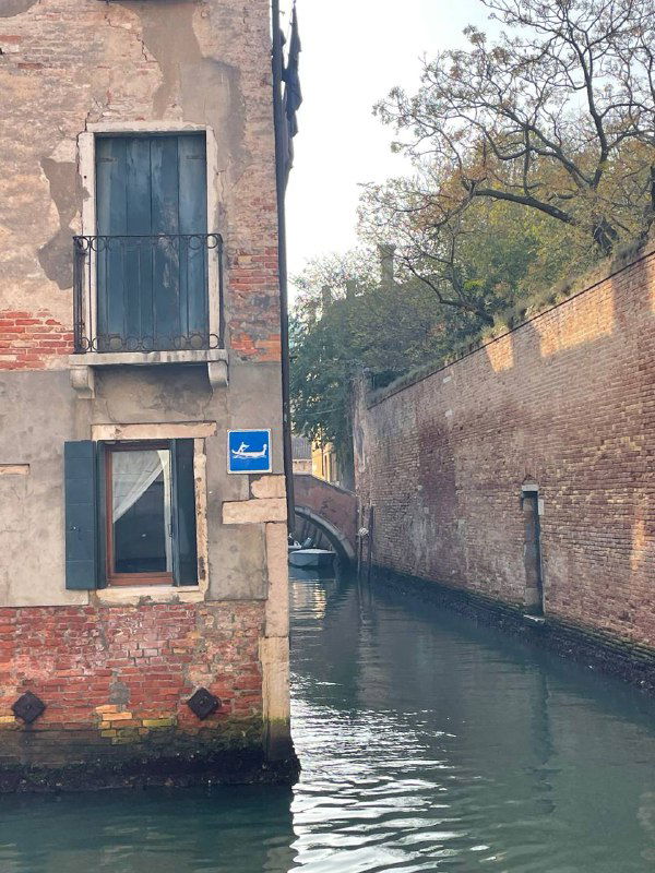 Угол узкого канала между старыми домами, вид на воду и небольшой пешеходный мост в городской тиши среди домов.