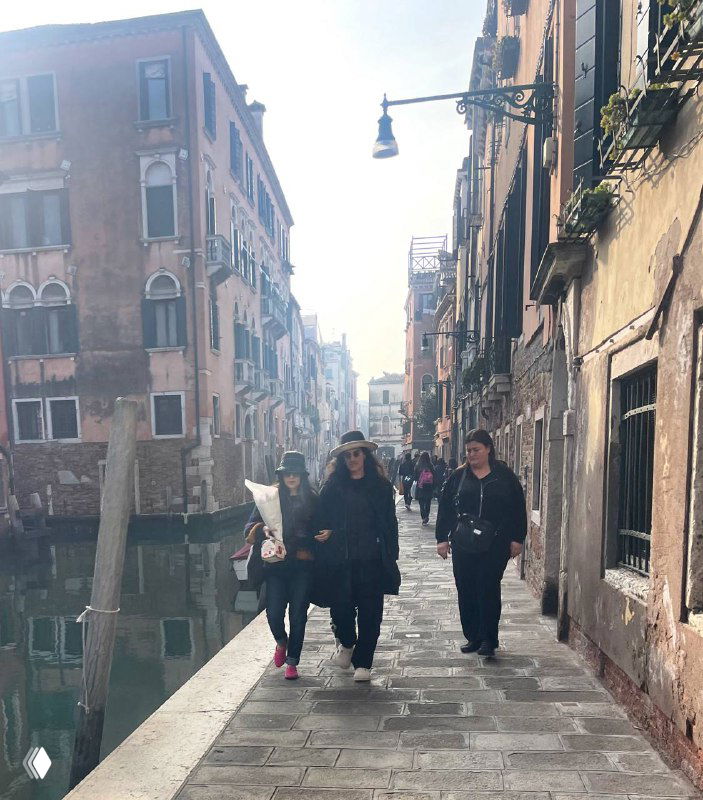 Набережная вдоль канала с множеством туристов и местных, которые идут по тротуару рядом с водой; оживлённая прогулочная сцена.