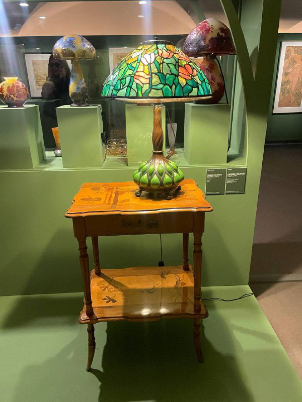 Детальный снимок одной из витрин: большая витражная лампа на деревянном столике в экспозиции ар‑нуво в Museo degli Innocenti.