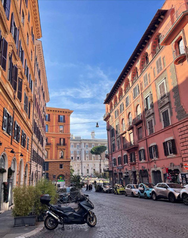 Узкая улица в Риме с типичными окрашенными домами, припаркованным скутером и голубым небом — прогулочный вид рядом с туристическими зонами.