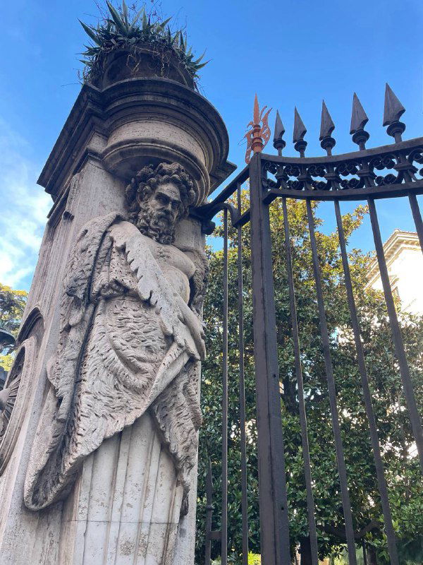 Каменная статуя и частая кованая ограда римского сада или парка — декоративная архитектурная деталь на прогулке по городу.