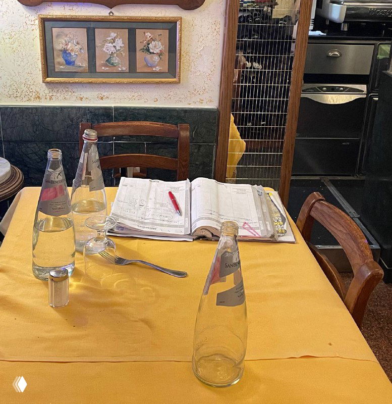 Жёлтый стол в траттории с бутылками воды, чашками и записной книгой — кадр во время обеда и подсчёта расходов в путешествии.