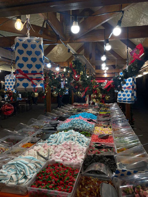 Палатка с яркими сладостями и мармеладом на рождественском рынке, ряд лотков с конфетами и подсветкой под навесом ярмарки.