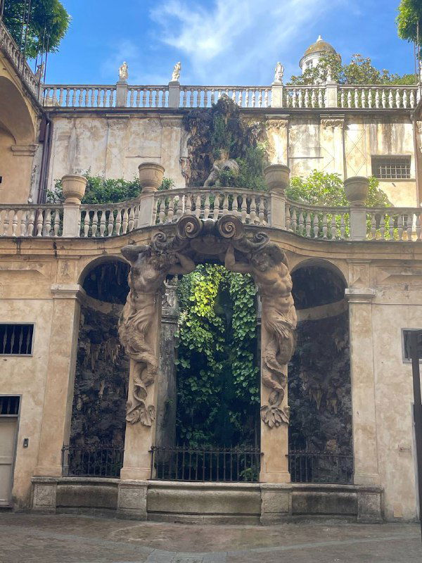 Декоративная каменная арка исторического здания в Генуе с барельефами и открытой террасой, часть старинной городской архитектуры.