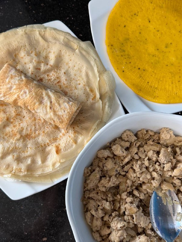 Подача: тарелки с тонкими блинчиками и миска с обжаренным куриным фаршем на темной столешнице — ингредиенты для начинки.