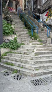 Бетонная наружная лестница в стамбульском районе с синими перилами, граффити и зеленью — пример ступеней, которые влияют на выбор маршрута.
