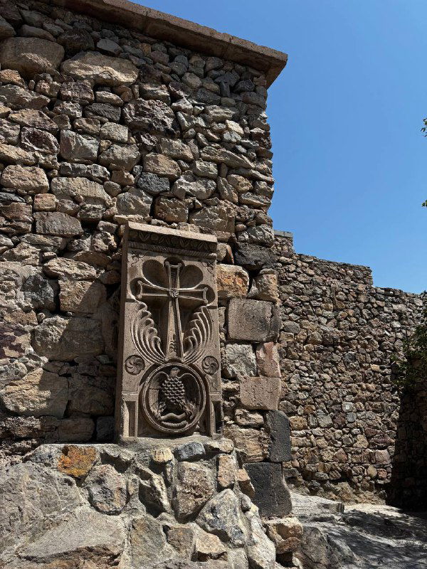 Крупный план старинной каменной резьбы и хачкара у стен монастыря Хор Вирап на фоне ясного голубого неба.