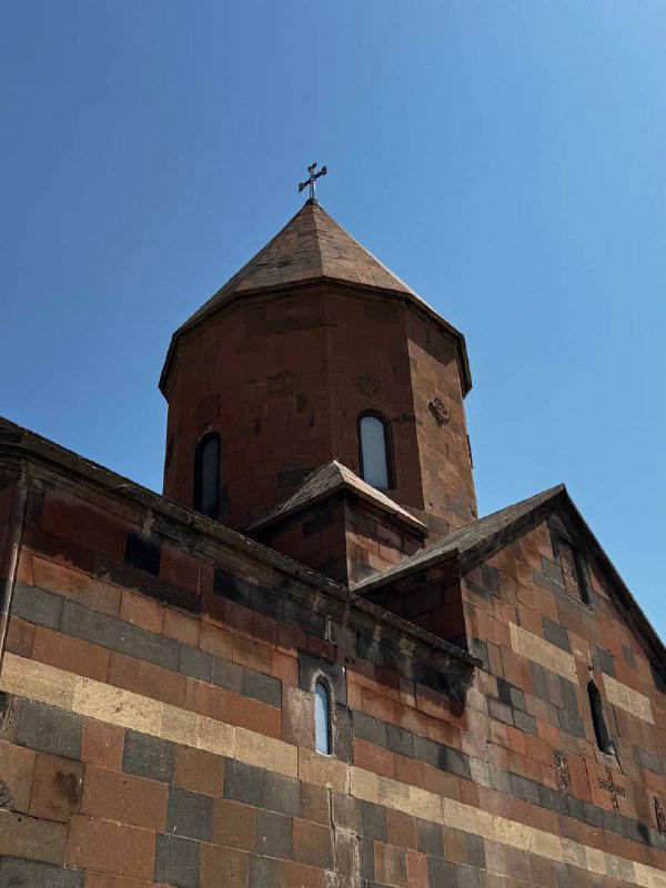 Фрагмент армянской церкви Хор Вирап: купол и цветная кладка из туфа на фоне чистого неба, вид снизу вверх.