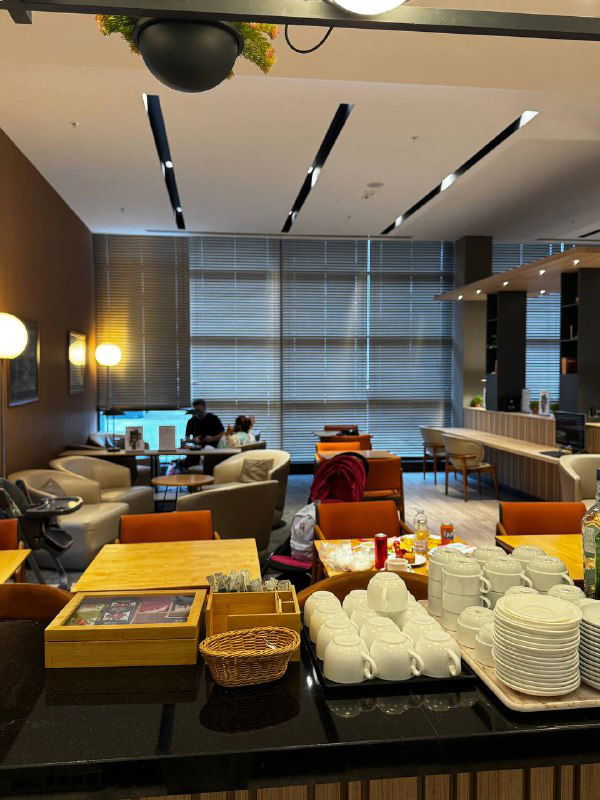 Шведский стол в лаунже аэропорта Батуми: чашки, тарелки и закуски на итогационной стойке, рядом мягкие кресла и панорамные окна.