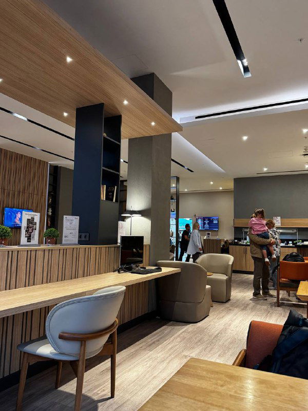 Уголок лаунжа в аэропорту Батуми с посадочными местами, телевизорами и стойкой — пассажиры располагаются и ожидают рейсы в комфортной обстановке.