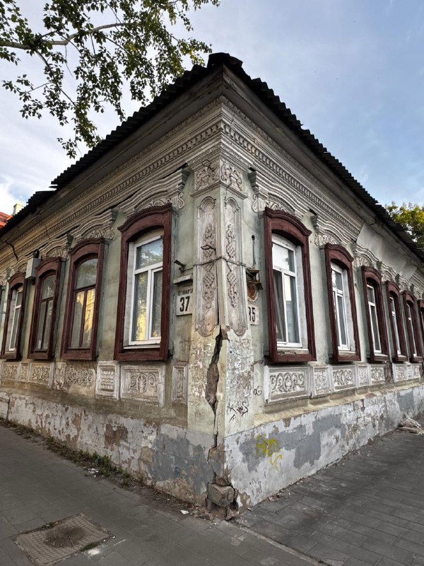 Угловой старинный дом в Оренбурге с лепниной и заметной вертикальной трещиной; часть фасада недавно замазана — городской архитектурный фрагмент