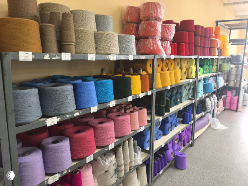 Ряды катушек и мотков пряжи разных цветов и текстур на стеллажах фабрики — вид ассортимента для шапок, шарфов и пледов.