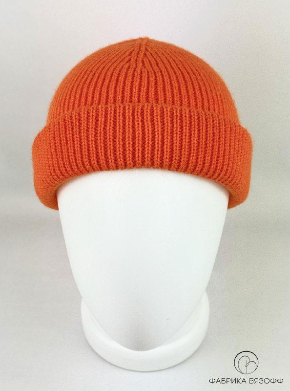 Оранжевая вязаная шапка на белом манекене; насыщенный цвет и выраженная рельефная структура вязки, студийная съёмка.