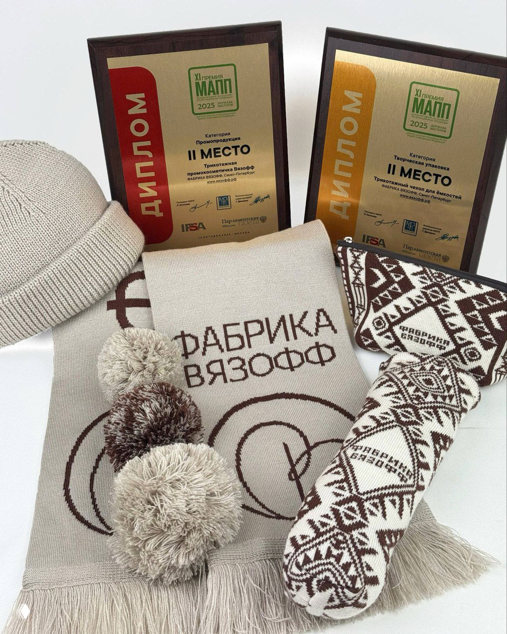 Дипломы Премии МАПП рядом с вязаной продукцией Фабрики ВЯЗОФФ: шапка, шарф с помпонами и узорный носок — образцы промопродукции и упаковки.