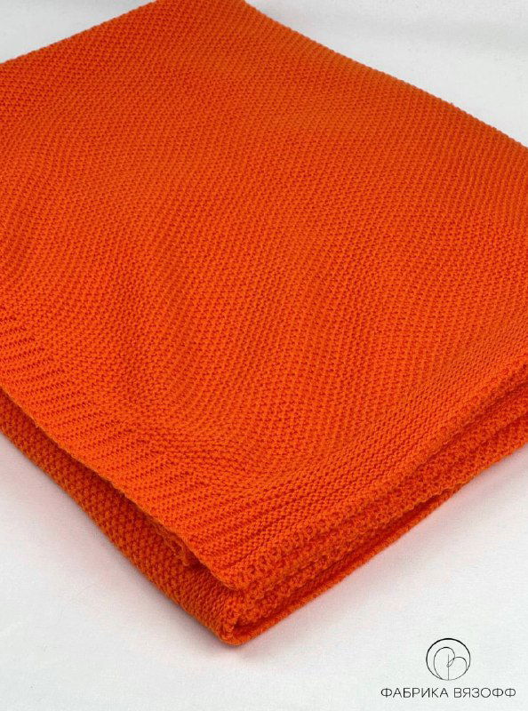 Плед оранжевого цвета аккуратно сложен на светлом фоне; кадр подчёркивает ровную поверхность и однородность цвета полотна.