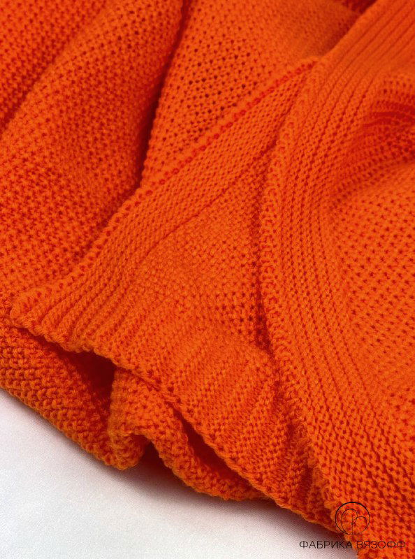 Крупный план драпировки оранжевого пледа: видны детали переплетения, мягкая драпировка и аккуратная отделка кромки изделия.
