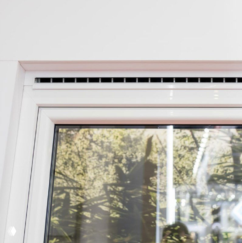 Фото окна с установленным клапаном и видом на зелёные деревья за окном — иллюстрация работы приточной системы без открывания створок.